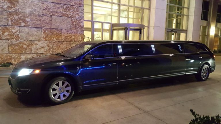 Black luxury limousine parked outside modern building at night.