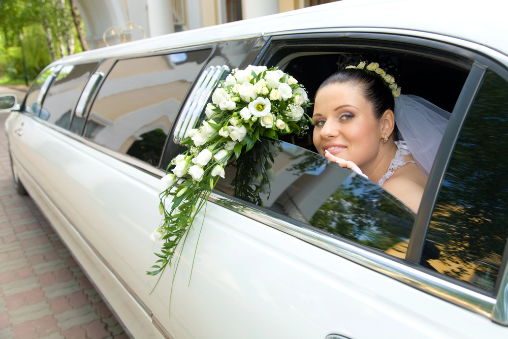 Bride with bouquet leaning out of limousine window