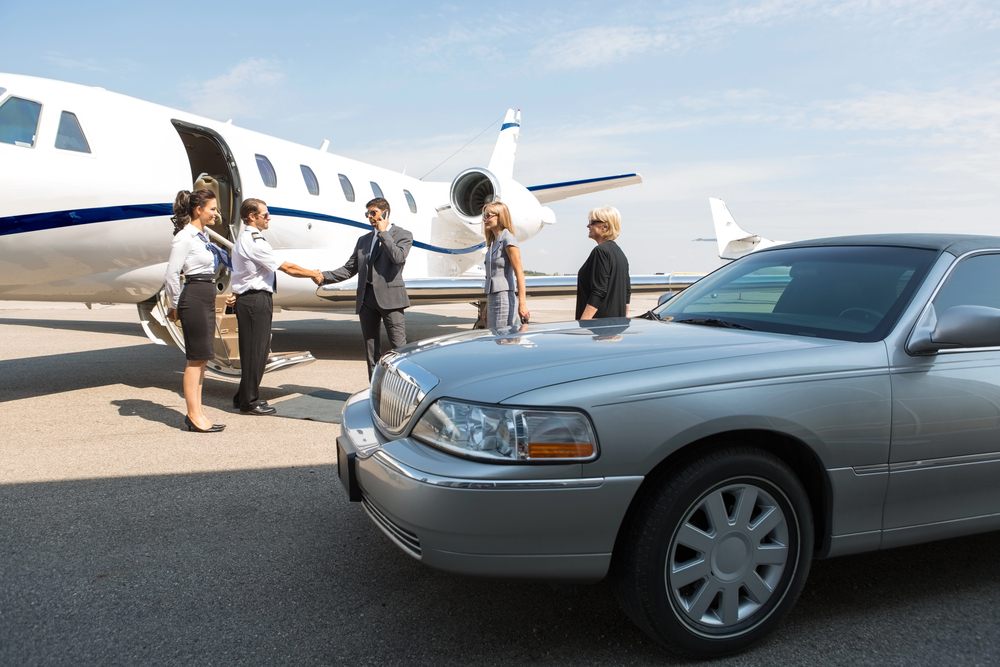 Businesspeople greeting beside private jet and luxury car