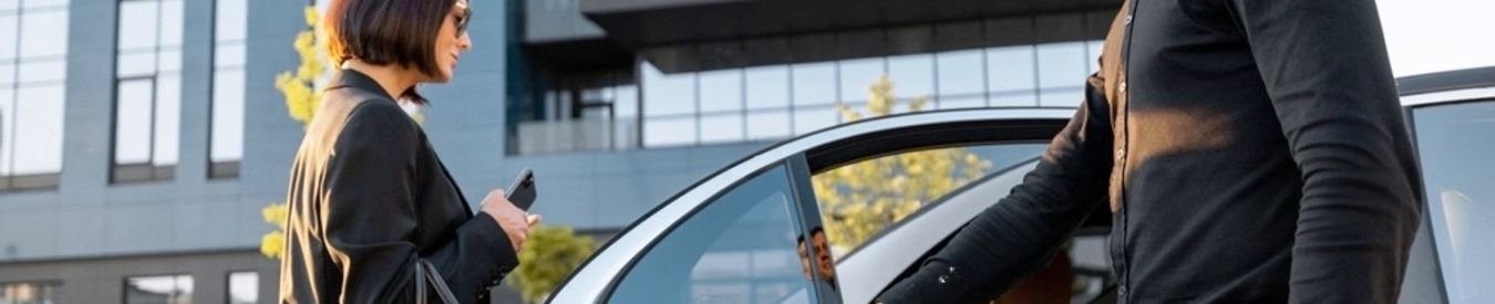 How Much Does A Chauffeur Cost? - Man opening car door for woman in business attire.