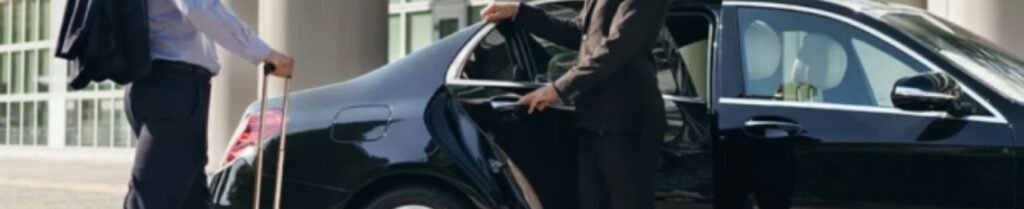 Driver opening car door for passenger with suitcase.