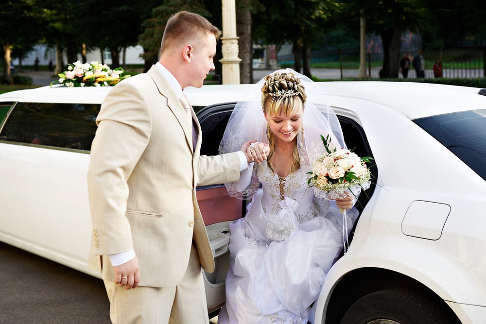 Bride exits limousine helped by groom.