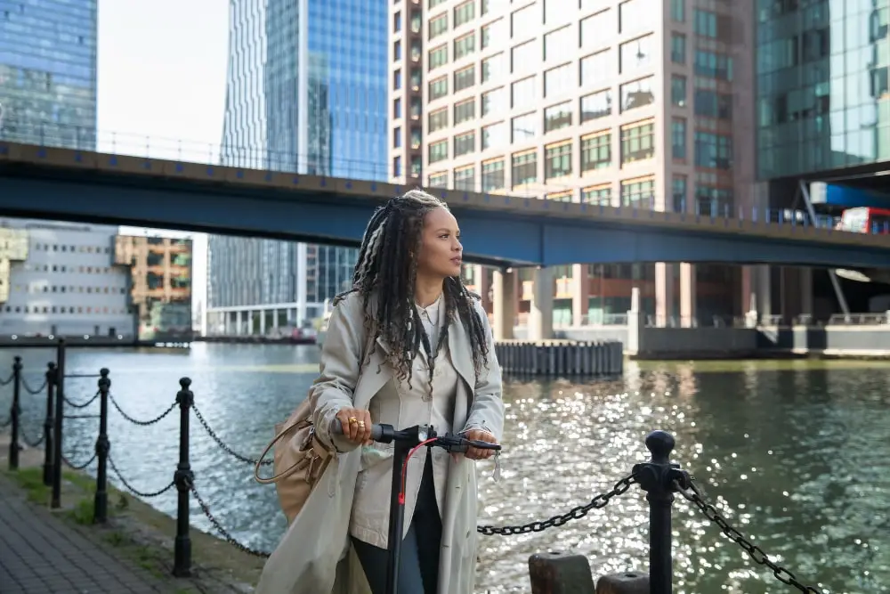 Person with scooter by urban waterfront.