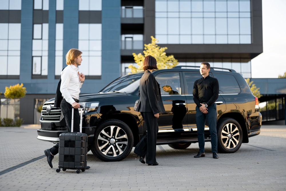 Group meeting near black SUV outside a building.