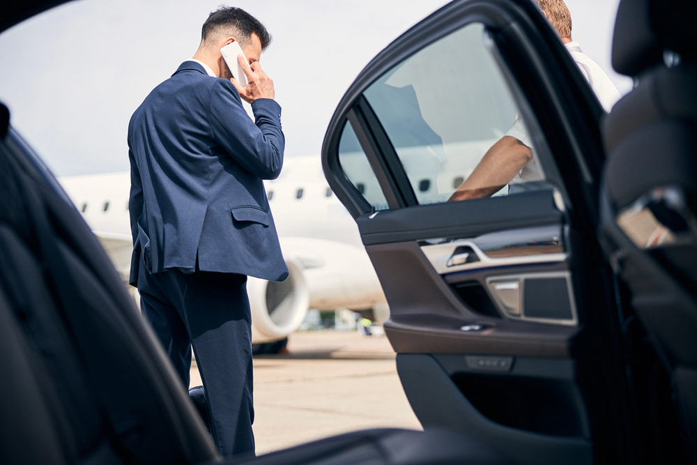 Businessman on phone near car at airport.